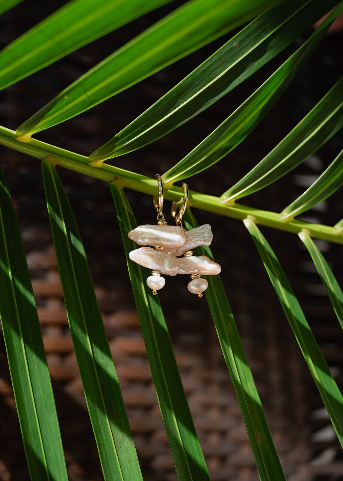 Elegant pearl drop earrings displayed on palm leaf, luxury Hawaiian pearl jewelry
