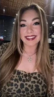 A smiling woman with long blonde hair wearing a leopard print top and a cross necklace, indoors at night.