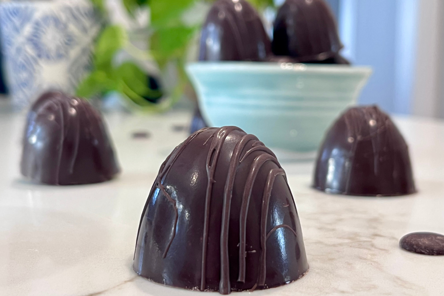 Dark chocolate truffles with a glossy finish and thin chocolate drizzle, arranged on a white surface.
