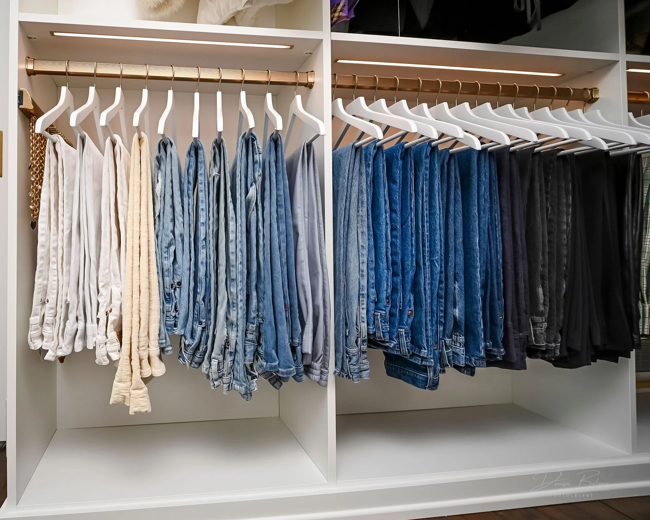 Display of jeans and pants arranged by color on white shelves in a clothing store.