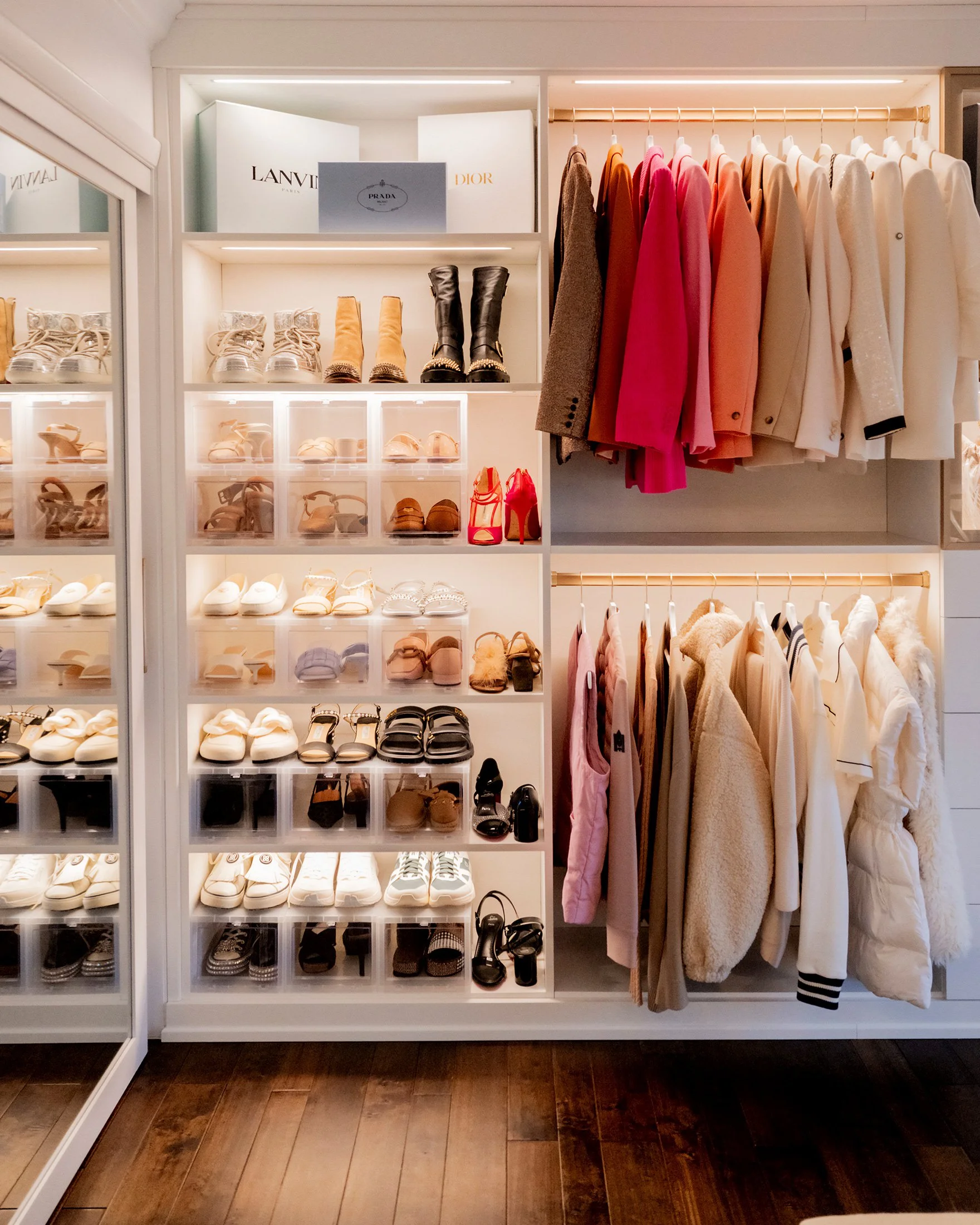 A retail store display with shelves of shoes and hanging outfits. Top shelf holds designer brands' boxes. Shoes in clear containers include sandals, boots, heels, sneakers, and flats. To the right are racks of women's coats, jackets, and dresses in v