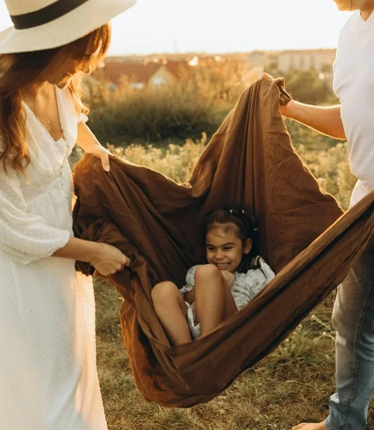 young girl swinging in a blanket held by two smiling people