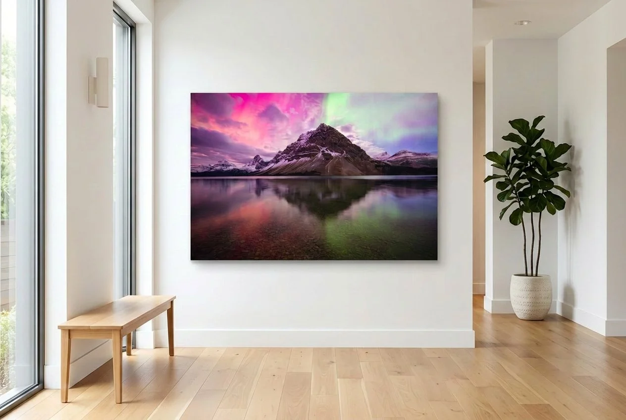 Interior of a modern room with a large landscape canvas depicting mountains and a colorful sky, a wooden bench, and a potted plant near a large window.