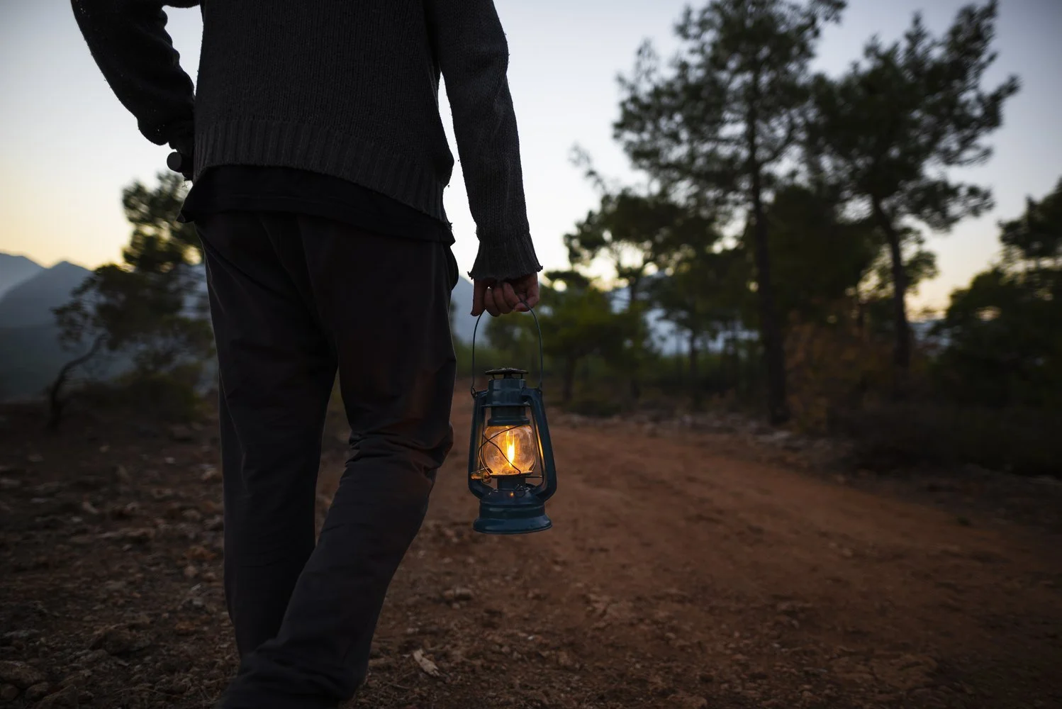 A person carrying a glowing lantern on a path at dusk, representing guidance and light on the spiritual journey