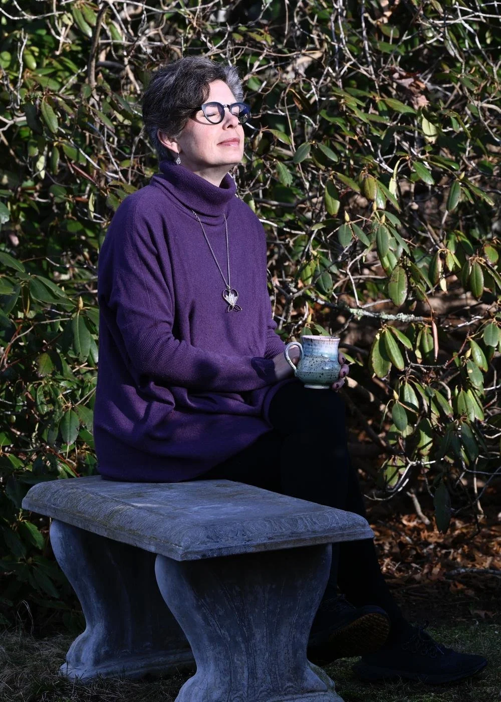 Libby Catania sitting in quiet contemplation on a garden bench, holding a cup of tea