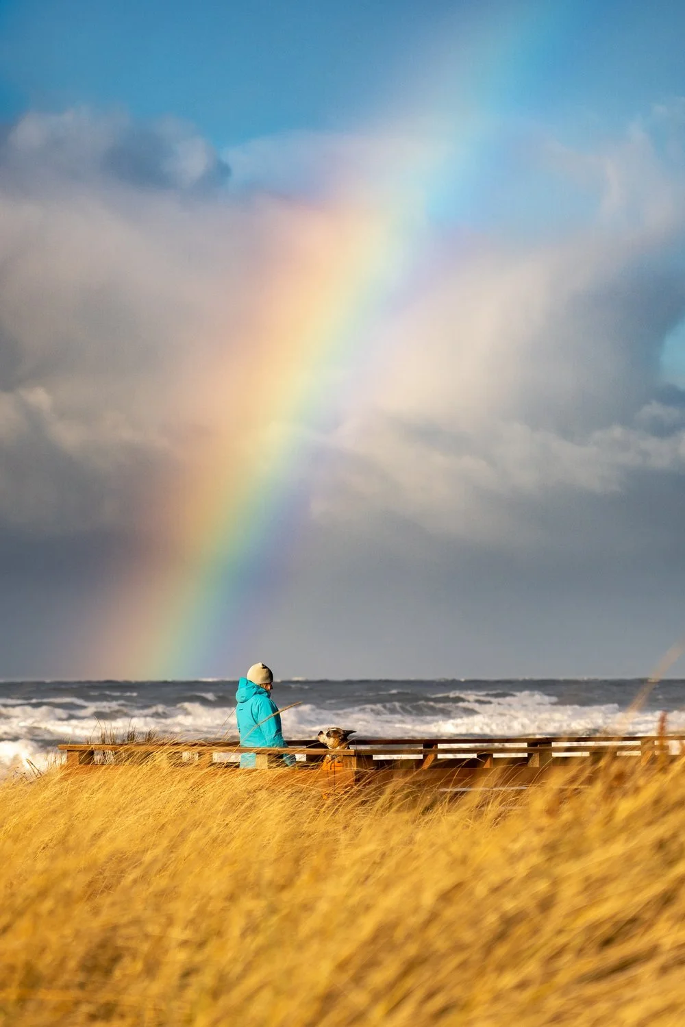 A person sitting peacefully before a rainbow over stormy seas, symbolizing hope and renewal after religious trauma