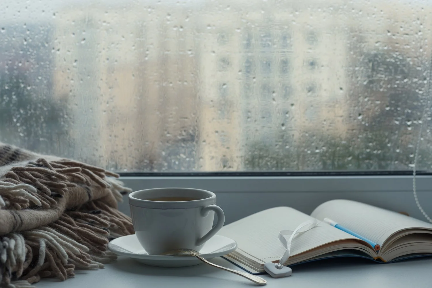 Open journal and cup of tea by a rainy window, representing reflective spiritual practice and soul care