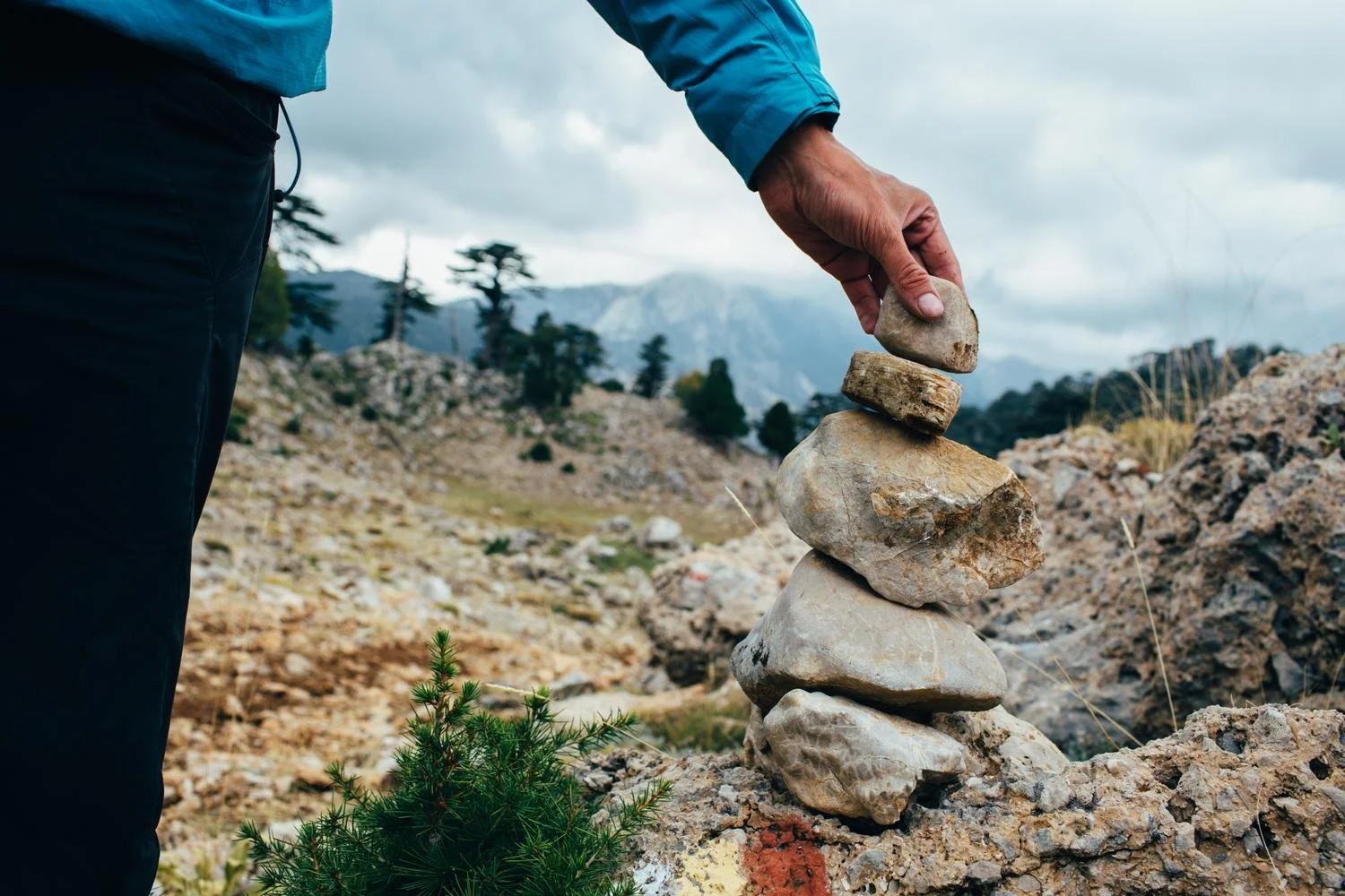 A person carefully stacking stones on a mountain path, representing intention, balance, and healing in the spiritual journey