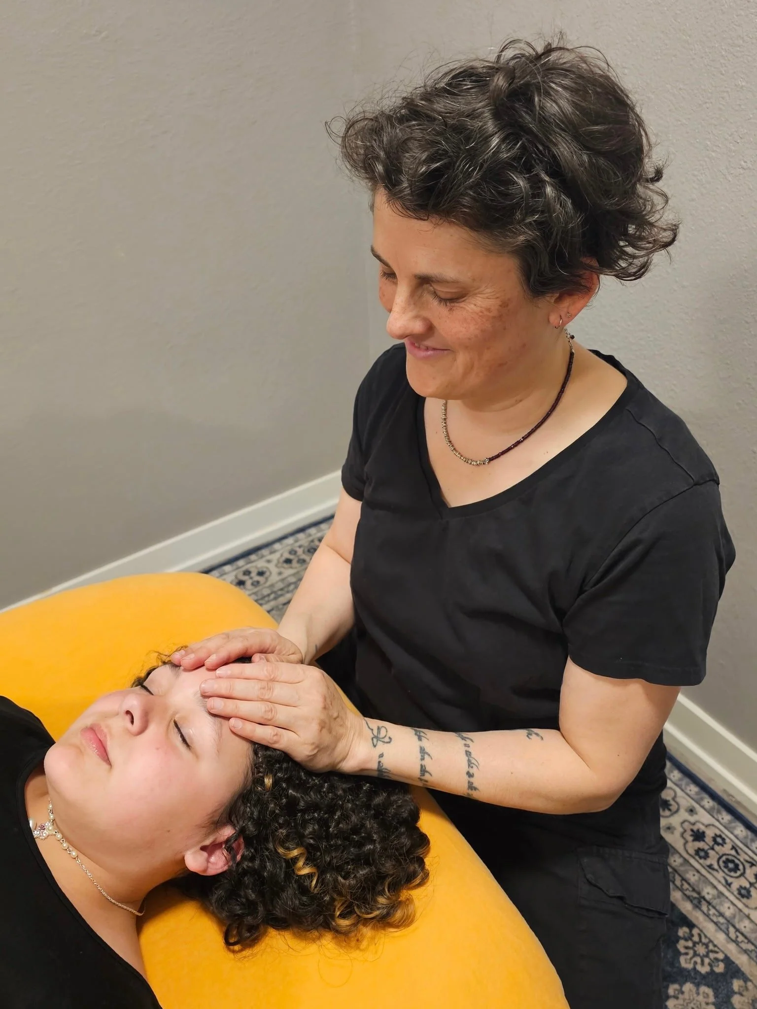 Woman with curly hair receiving a facial massage from a therapist in a comfortable setting.