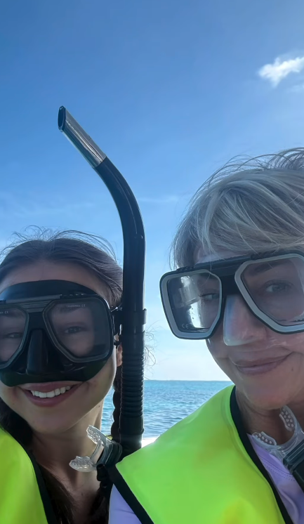 Two people wearing snorkeling masks and yellow life jackets stand near the ocean on a clear day.