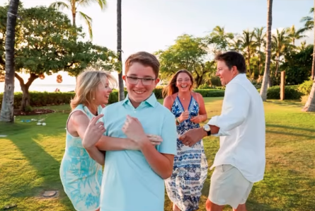 A family celebrating outdoors on a sunny day, with a young boy and three adults smiling and enjoying each other's company.