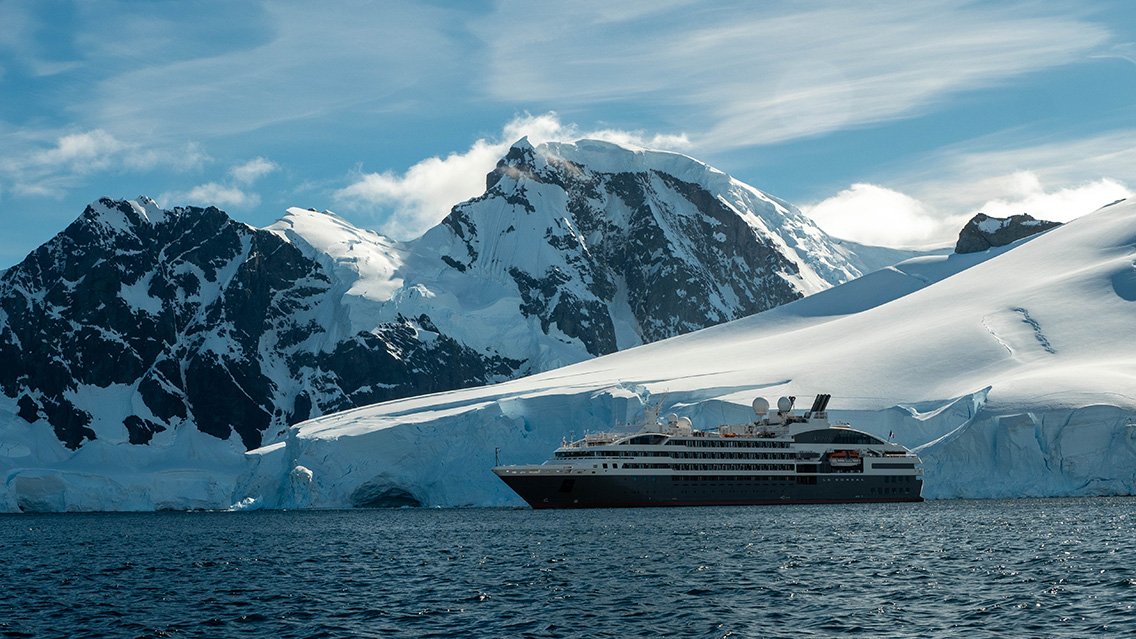 A cruise ship sailing near icy, snow-covered mountains in a polar region.