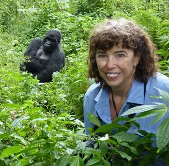 A woman smiling in a green forest with a gorilla behind her.