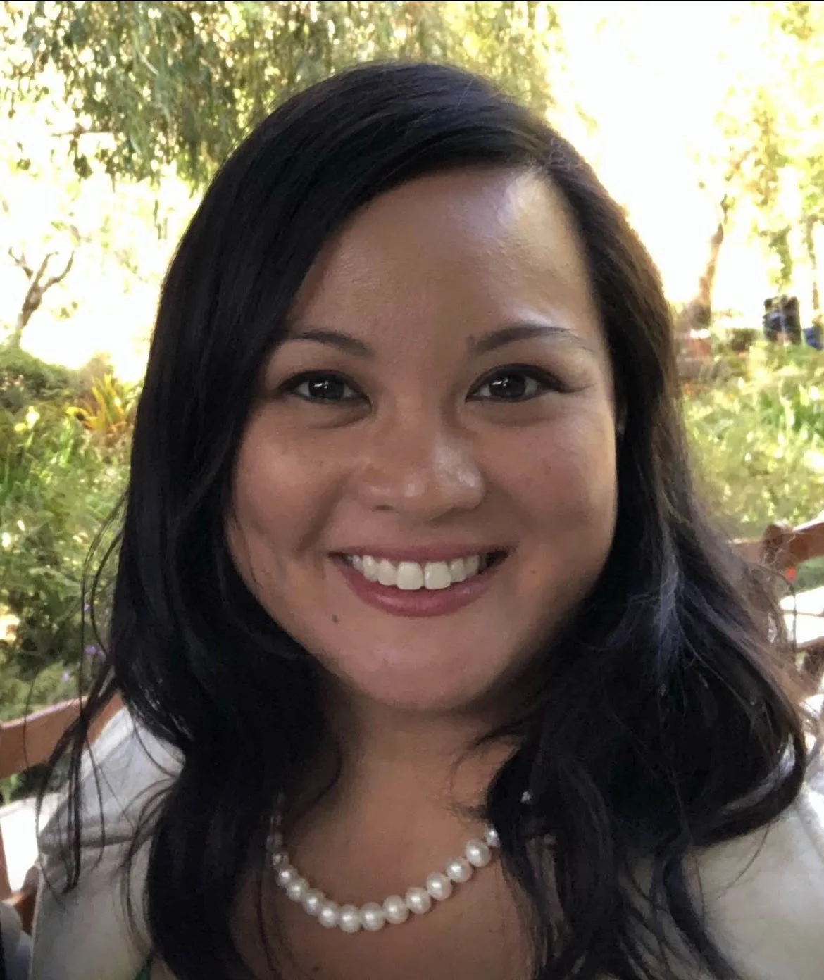 A marketing operations expert with long black hair smiling outdoors with trees and greenery behind her.