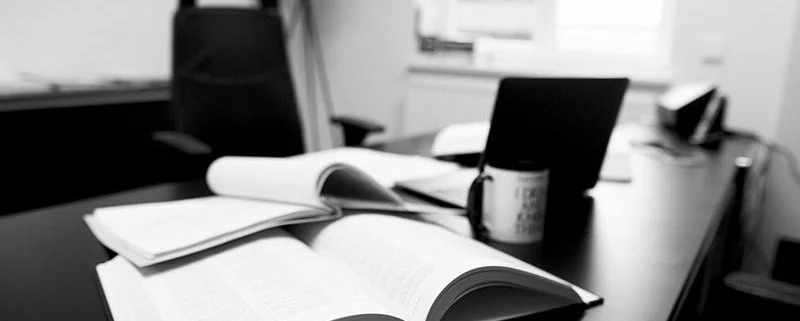 Escritorio con libros abiertos, una taza y una computadora portátil.