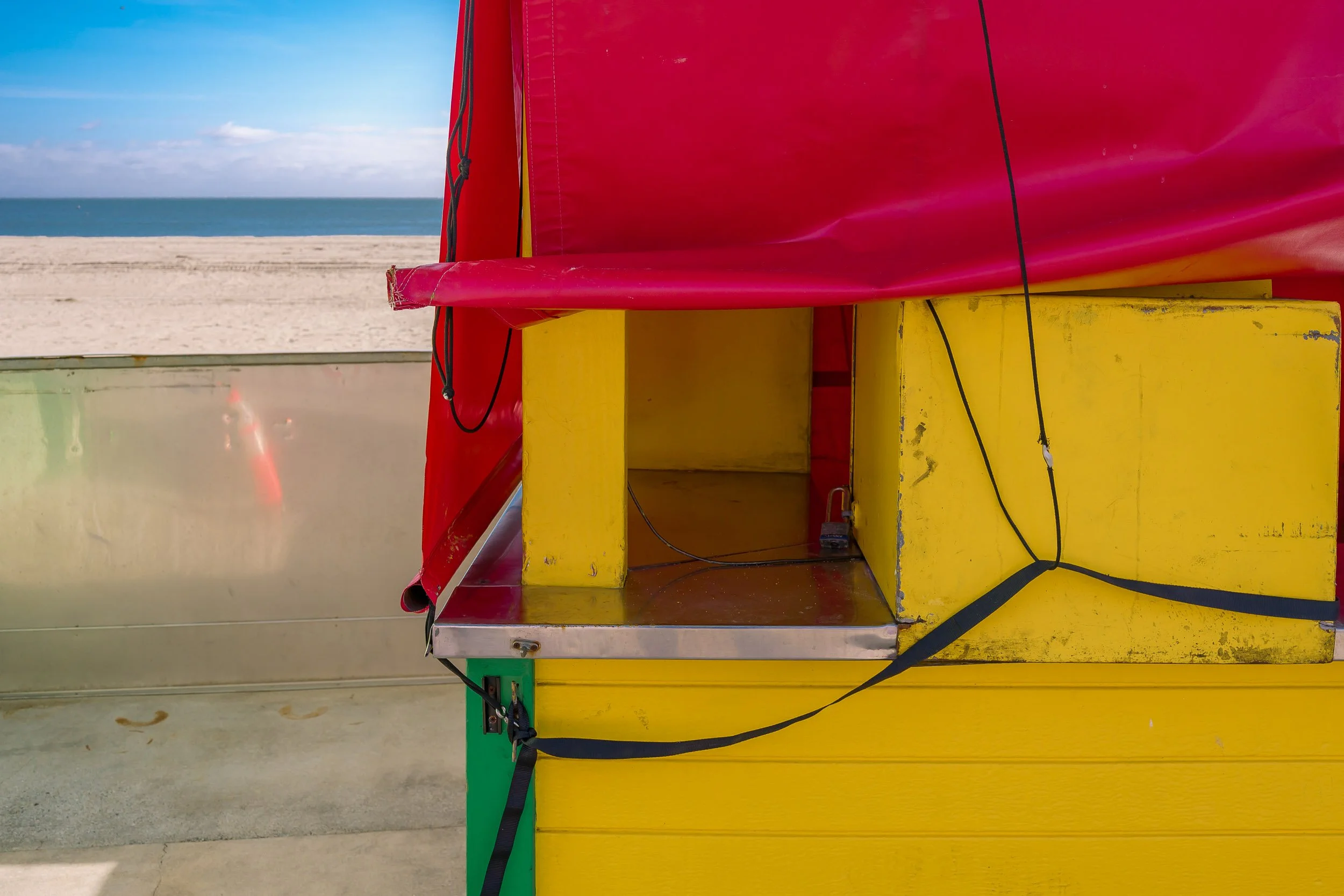 Close-up of a colorful lifeguard station with red, yellow, and green sections on a beach, with sand and ocean in the background.