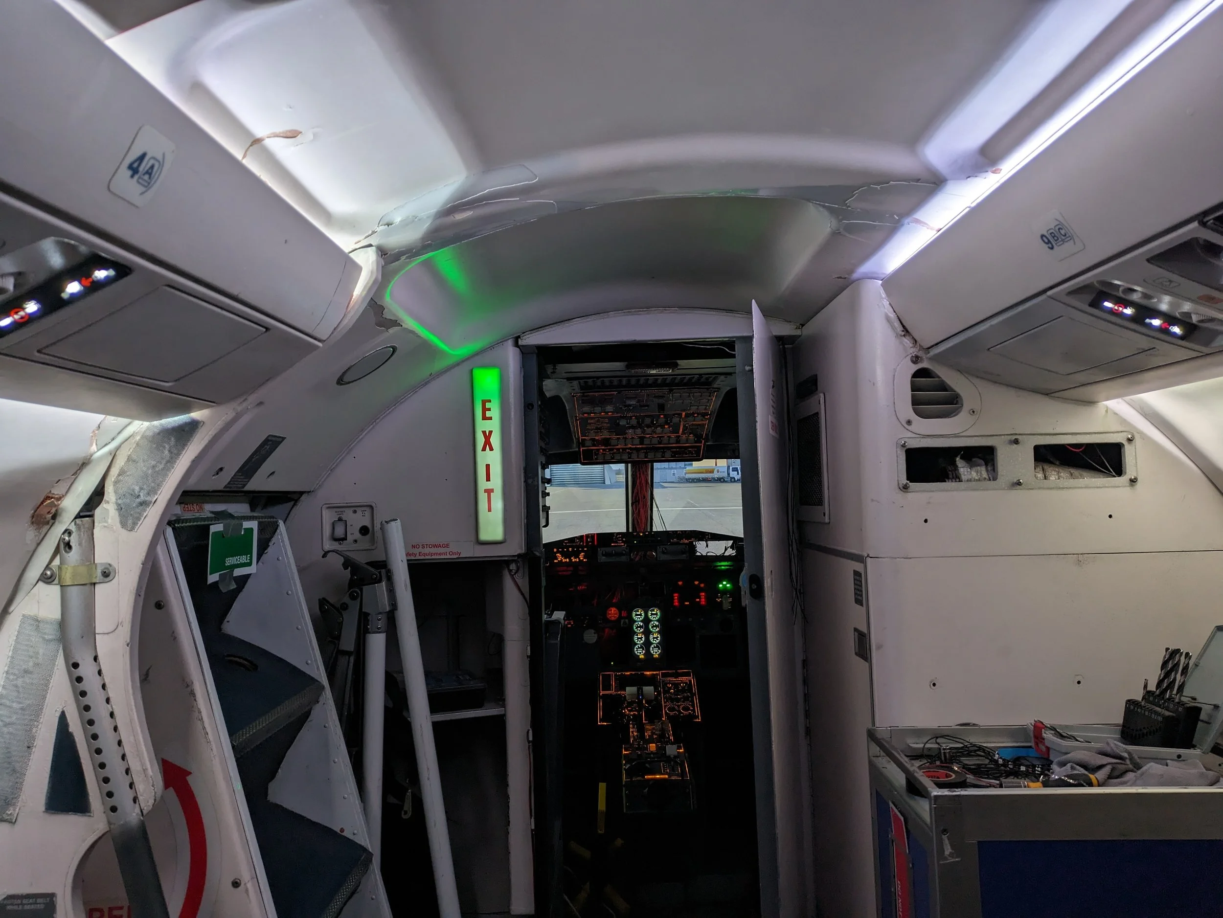 The interior of an airplane cockpit with damaged ceiling panels and exposed wiring.