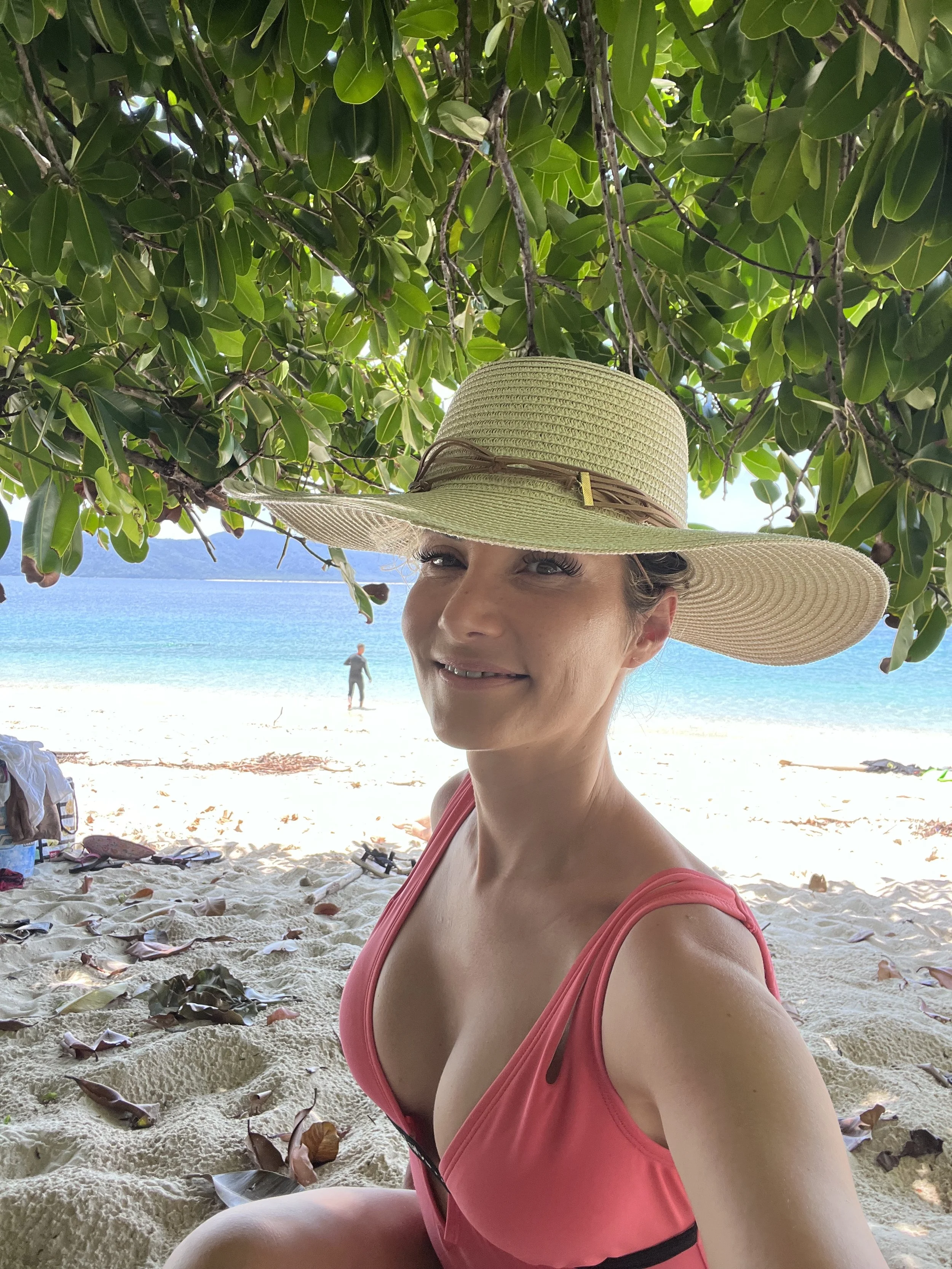 Woman in a straw hat on Nudey Beach at Fitzroy Island near Cairns with turquoise Coral Sea water, Queensland, Australia.