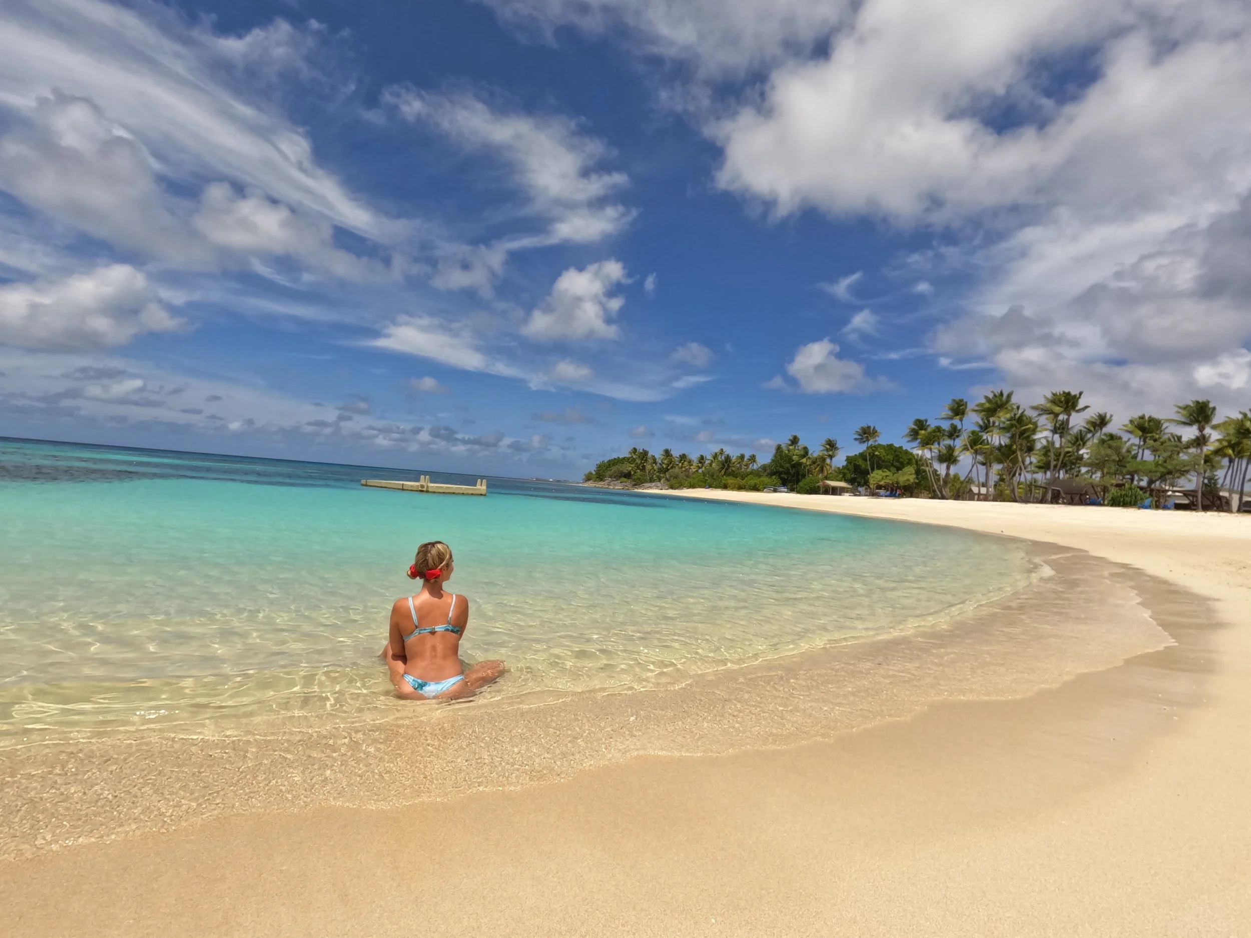Traveler sitting in turquoise lagoon on Kwajalein Atoll beach with palm trees and Pacific Ocean horizon