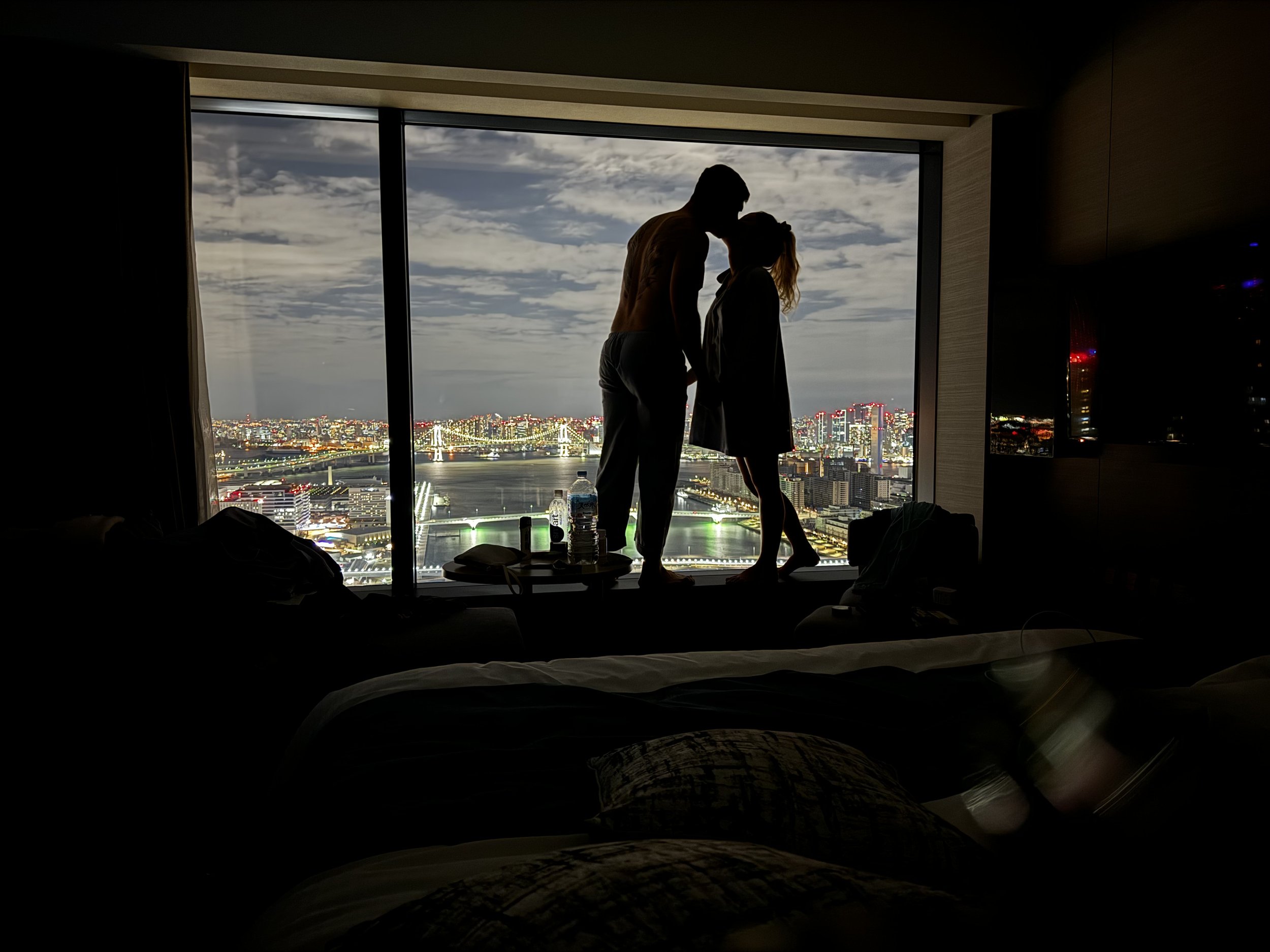 Couple enjoying a romantic moment overlooking Tokyo skyline and Rainbow Bridge at night from a hotel room in Japan.