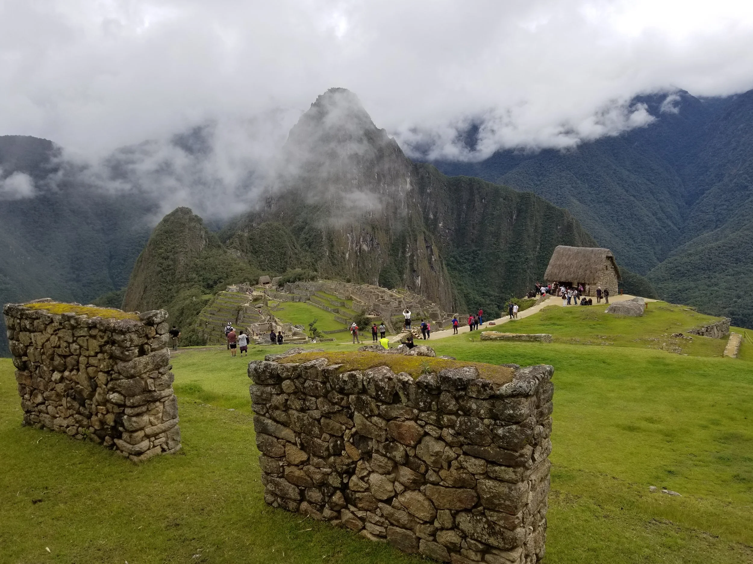 Visitors exploring the famous Guardhouse viewpoint above Machu Picchu with Huayna Picchu rising through the clouds behind the ancient Inca citadel.