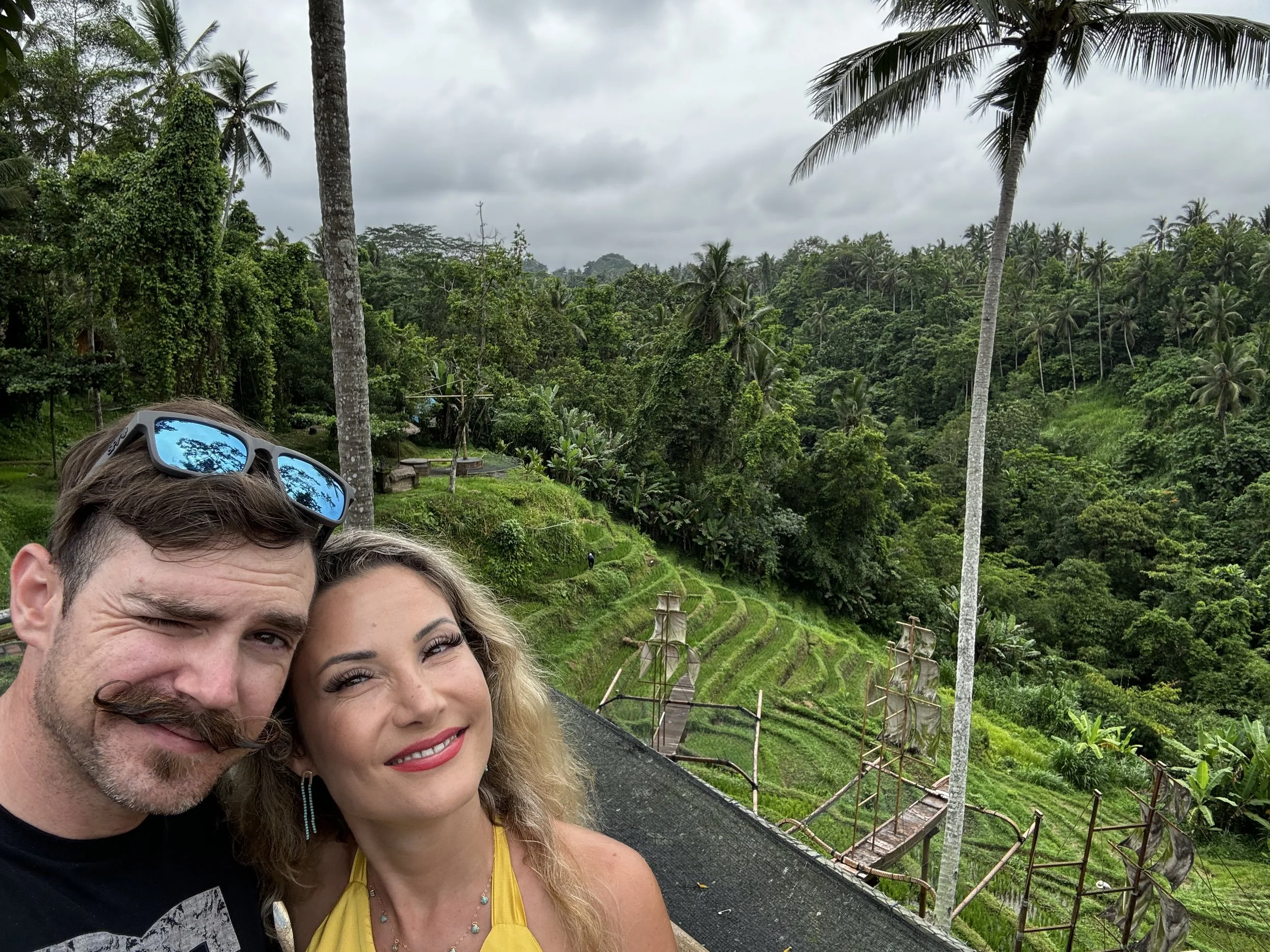 Travelers taking a selfie above the Tegalalang rice terraces with tropical jungle and palm trees near Ubud, Bali, Indonesia.