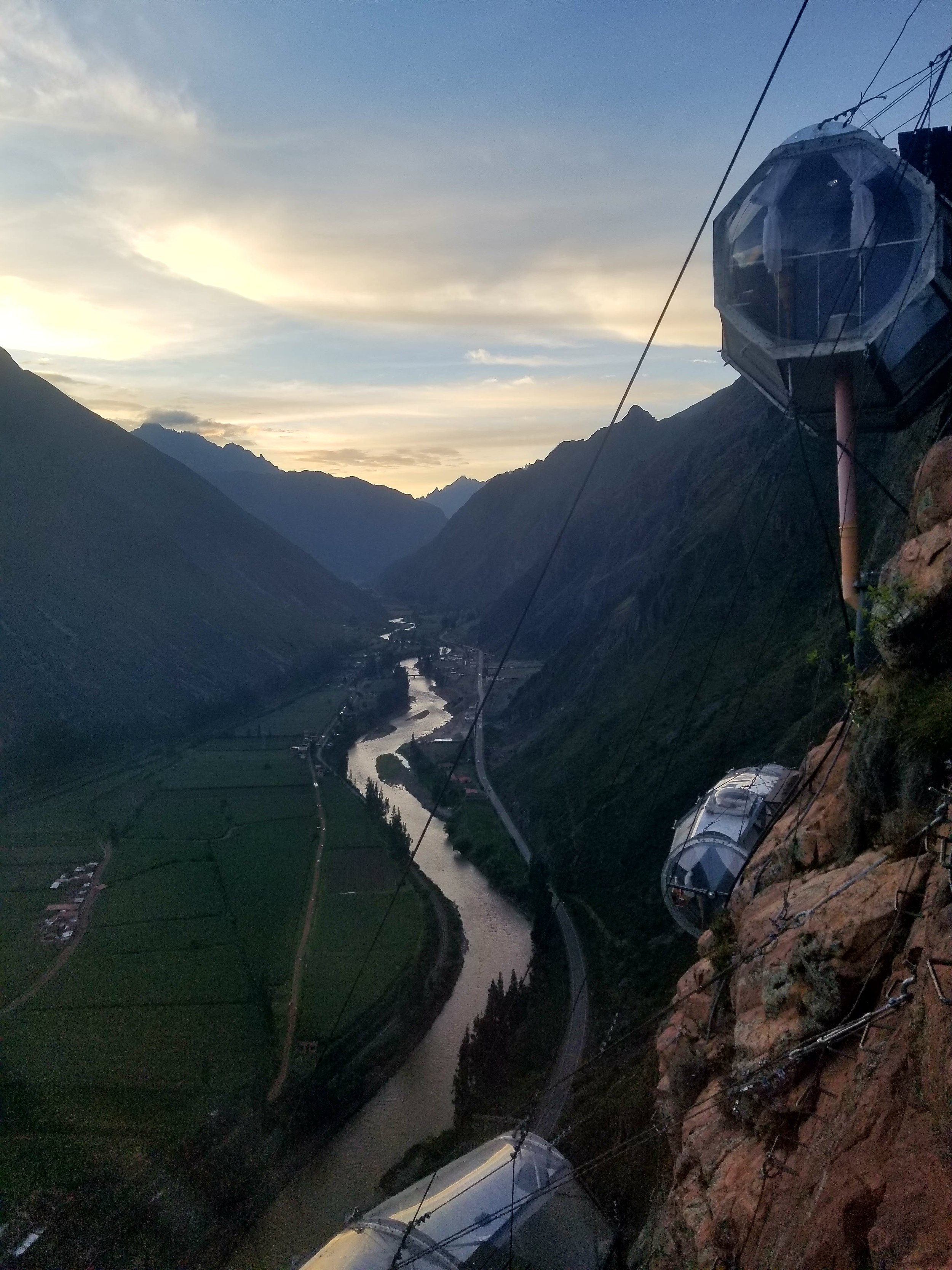 Skylodge Adventure Suites glass capsules suspended on a cliff above the Sacred Valley and Urubamba River near Cusco, Peru at sunset.