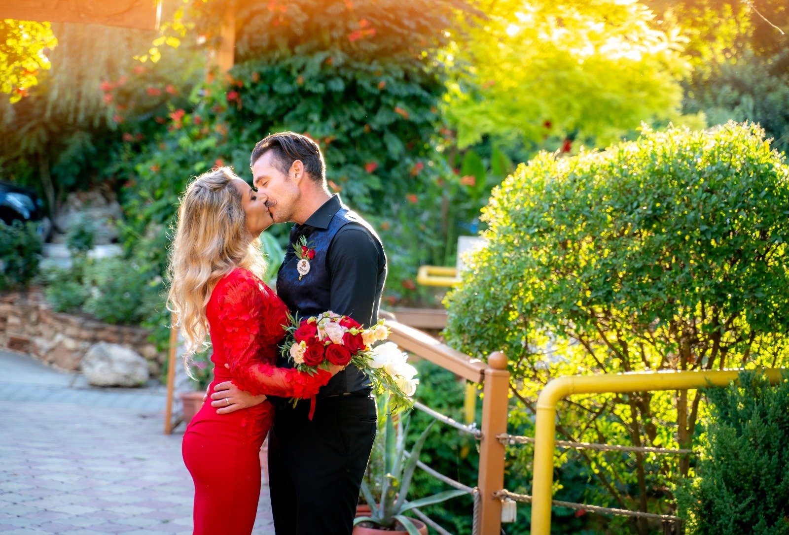 Bride and groom kissing in a garden during an outdoor wedding ceremony with flowers and greenery.