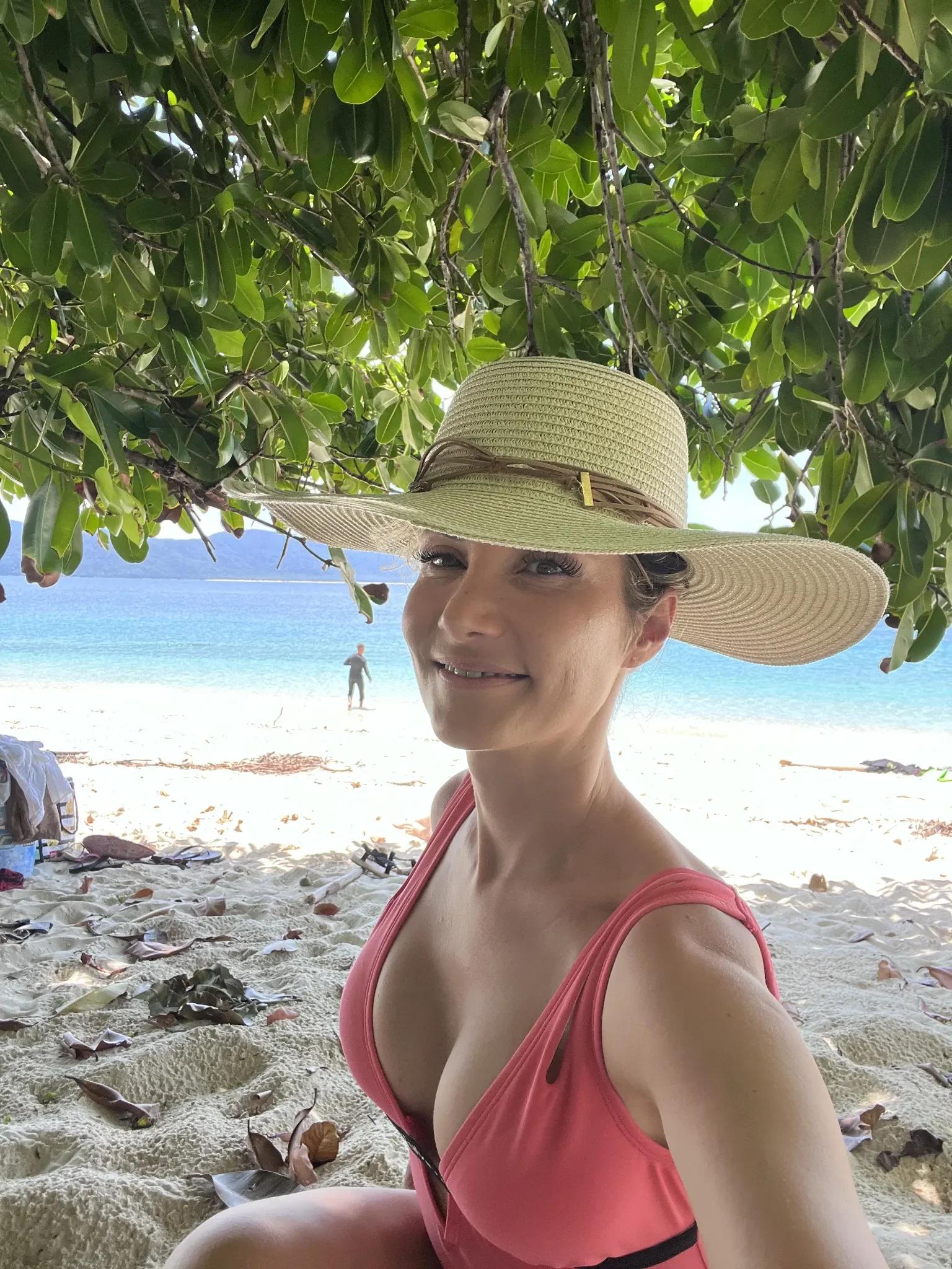 Woman in a straw hat on Nudey Beach at Fitzroy Island near Cairns with turquoise Coral Sea water, Queensland, Australia.