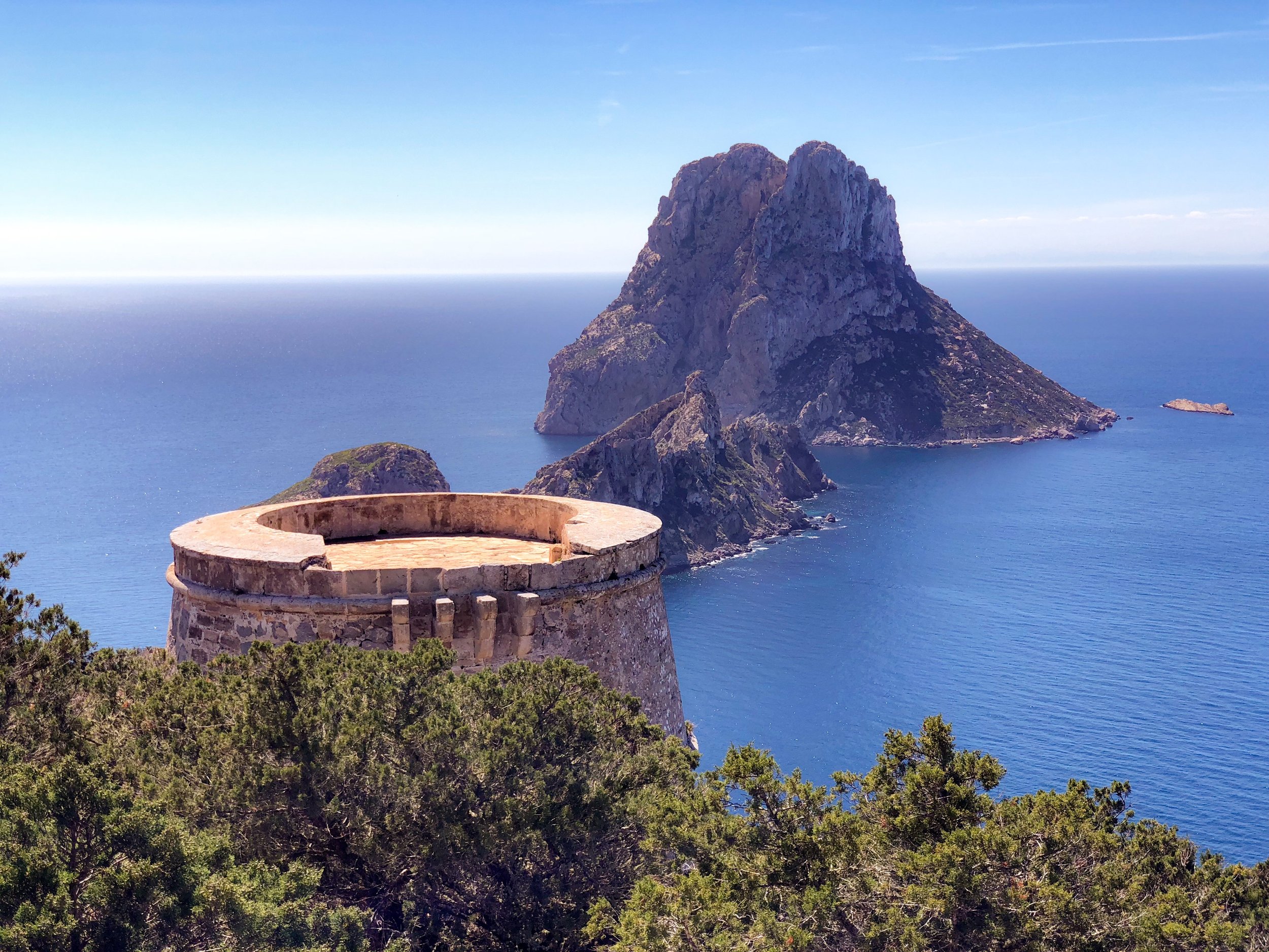 Historic Torre des Savinar watchtower with a view of the iconic Es Vedrà island rising from the Mediterranean Sea near Ibiza, Spain.