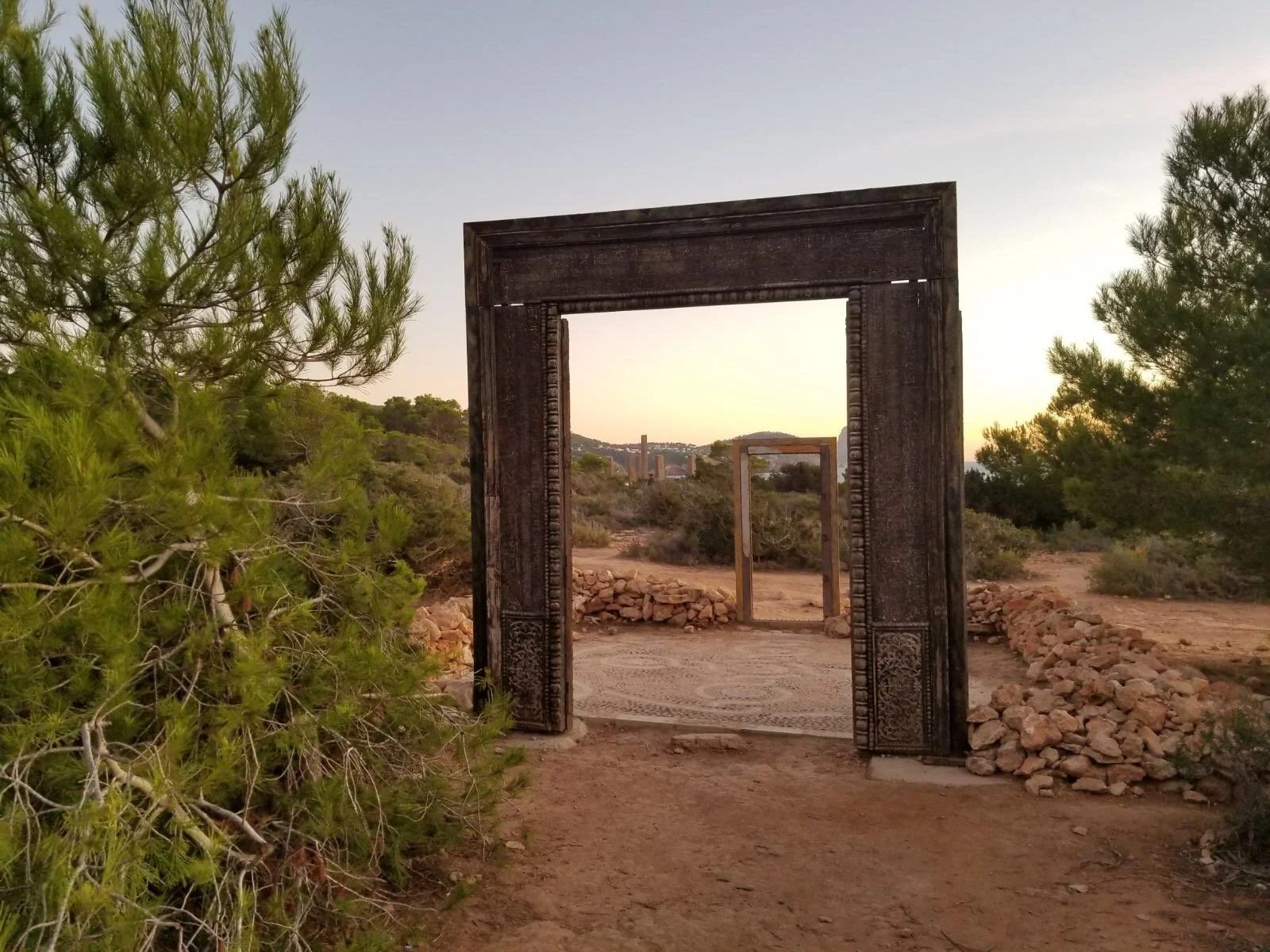 Freestanding doors and frames from the “Puertas de Cala Llentia” art installation in Ibiza, set among stone walls and pine forest.