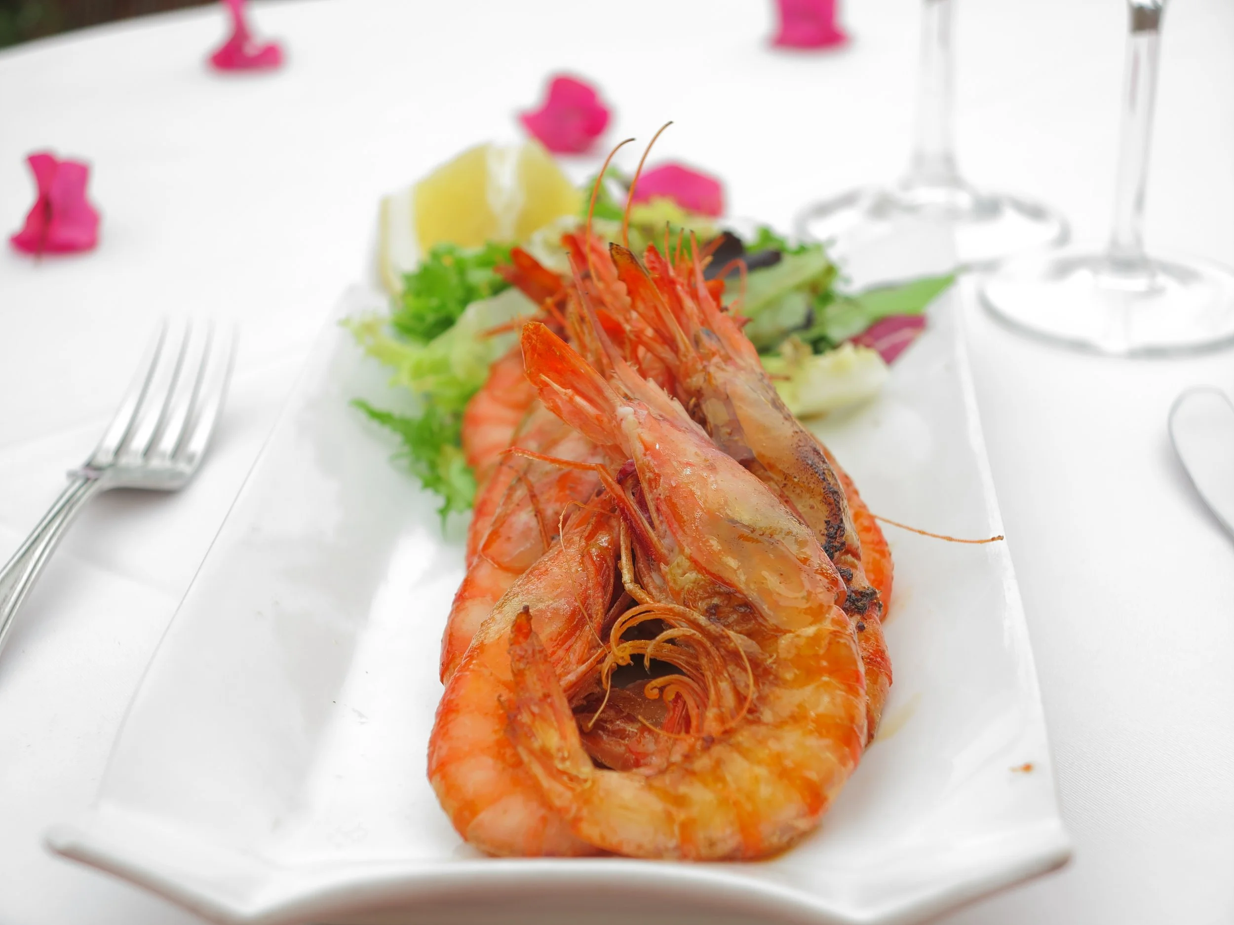 Plate of grilled Mediterranean red prawns from Ibiza served with fresh salad and lemon on a white table setting.