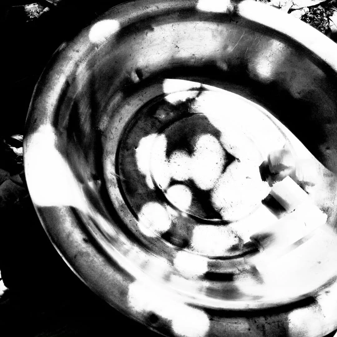 Une image en noir et blanc montrant un cadran de montre ou un objet circulaire métallique avec des reflets et des ombres, vue de dessus.