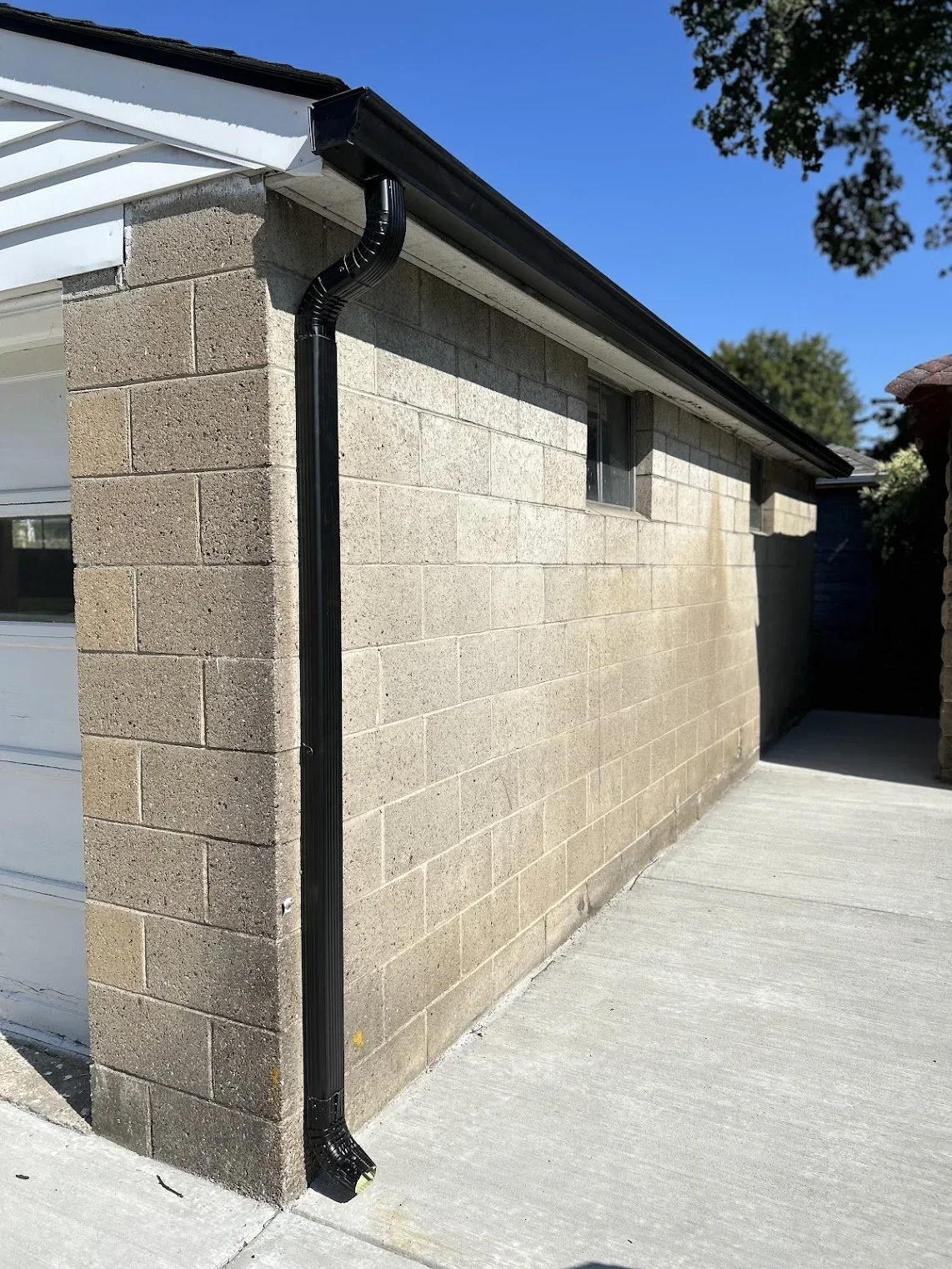 Exterior of a building with beige brick walls, a white garage door, a black gutter system, and a small window on the upper part of the wall, under a clear blue sky.