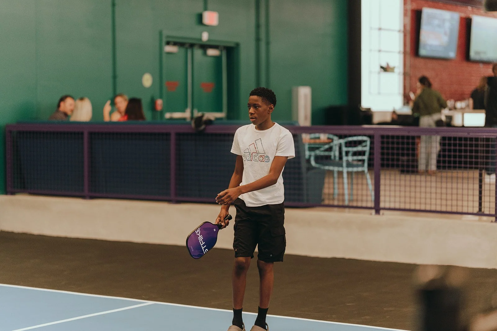 Four children standing on a tennis court holding paddles and wearing medals after a match or tournament.