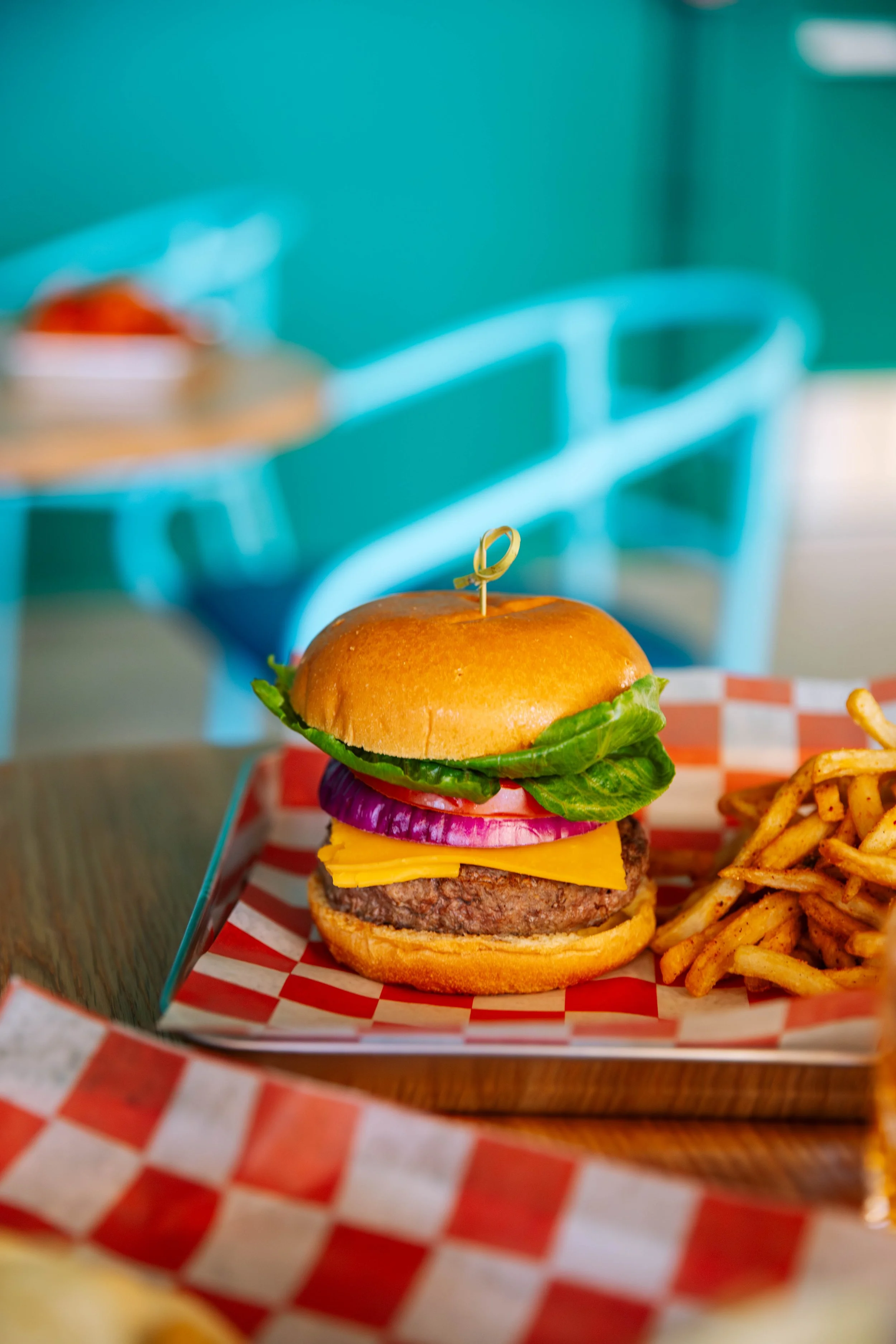 A cheeseburger with lettuce, tomato, onion, cheese, and a beef patty, served with French fries on a checkered paper tray.