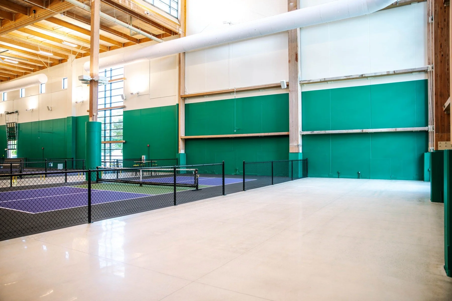 Indoor pickleball courts with purple courts, black fencing, green walls, and wooden ceiling beams.