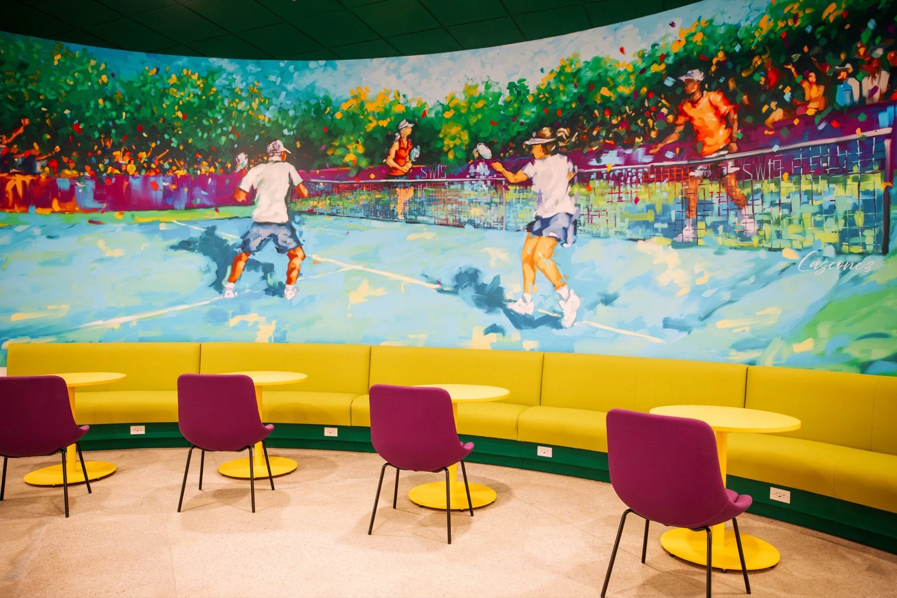 Colorful mural of people playing tennis on a court, seen from inside a modern lounge with yellow banquette seating and purple chairs.