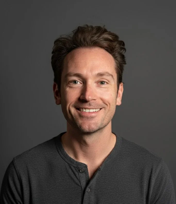 Portrait of a smiling man with brown hair, wearing a dark gray shirt, against a gray background.