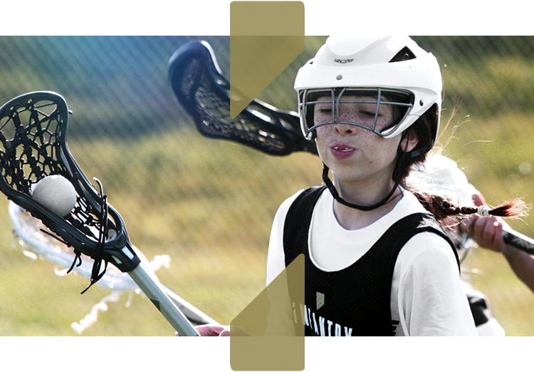 Youth lacrosse player wearing a helmet and holding a lacrosse stick during a game.