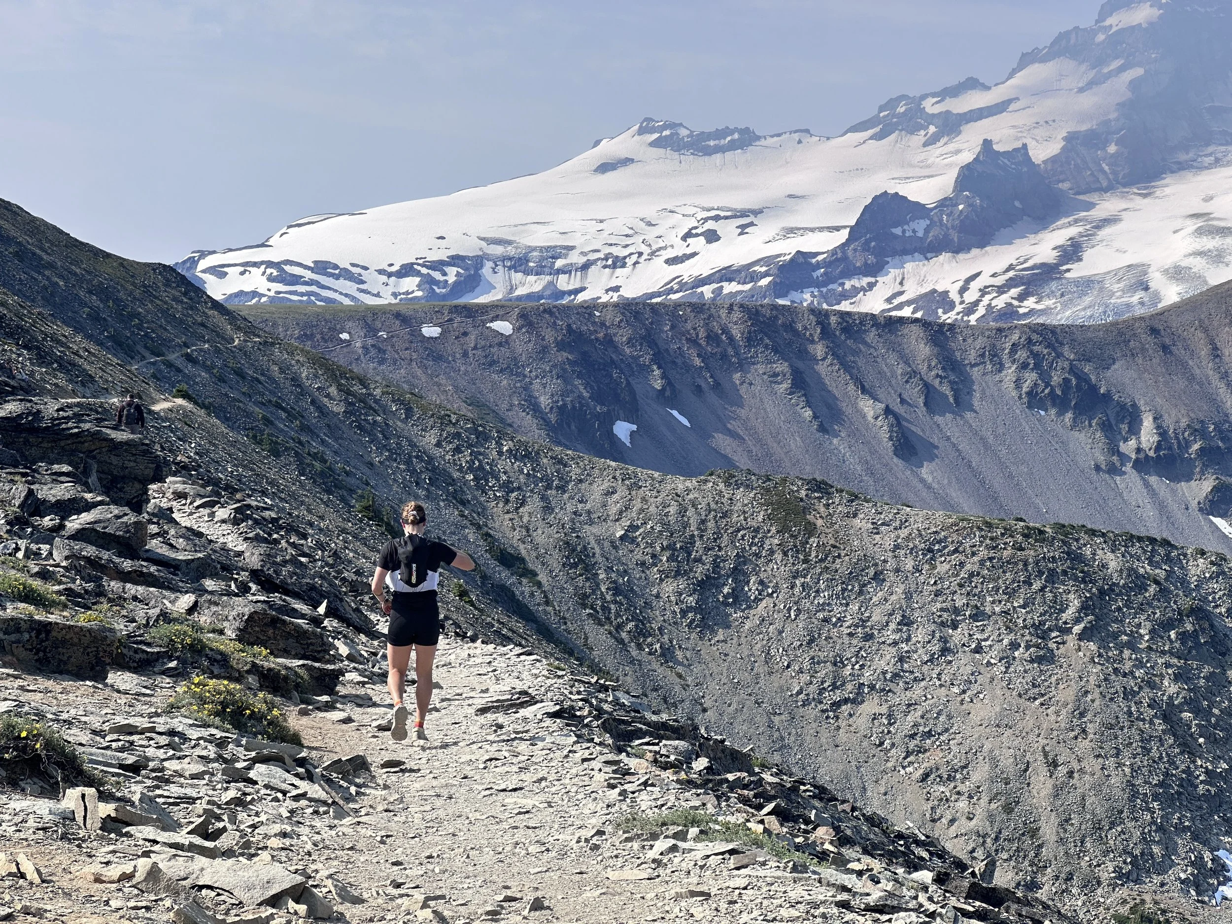 A person hiking on a rocky mountain trail with snow-covered peaks in the background.