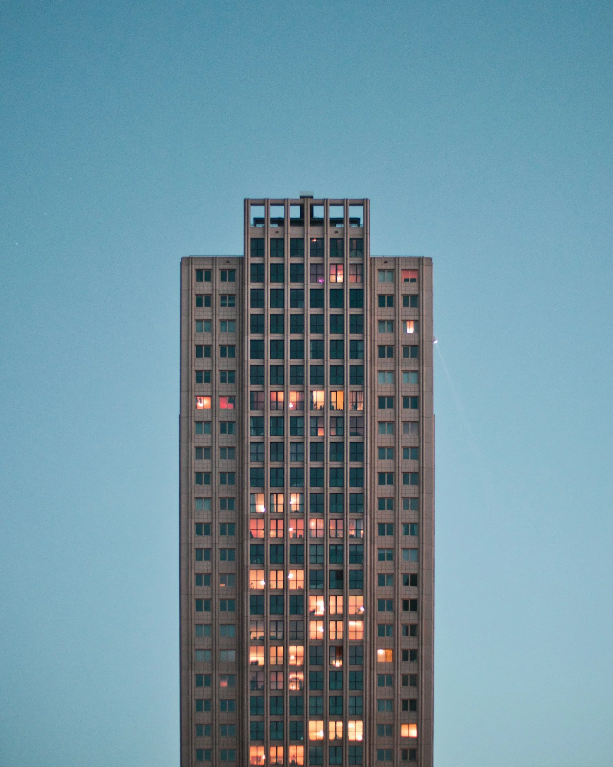 A tall office building with illuminated windows against a clear blue sky at dusk.