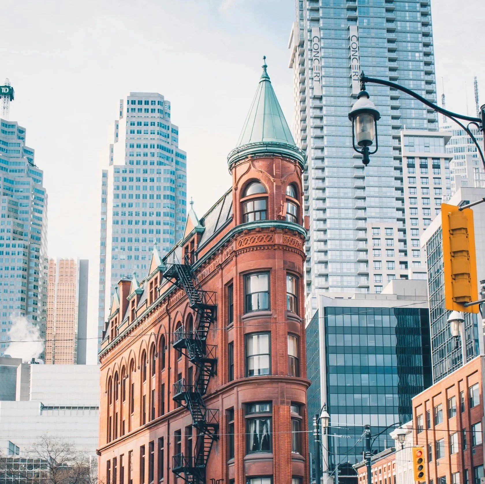 Red brick historic building with a turret and fire escapes set against modern high-rise buildings in Downtown Toronto.