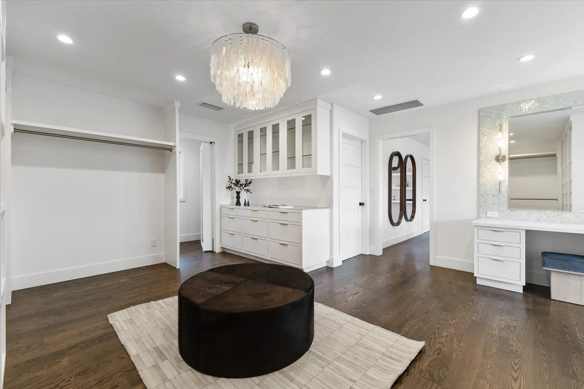 Modern white bedroom with built-in storage, a chandelier, a large mirror, and dark hardwood floors.