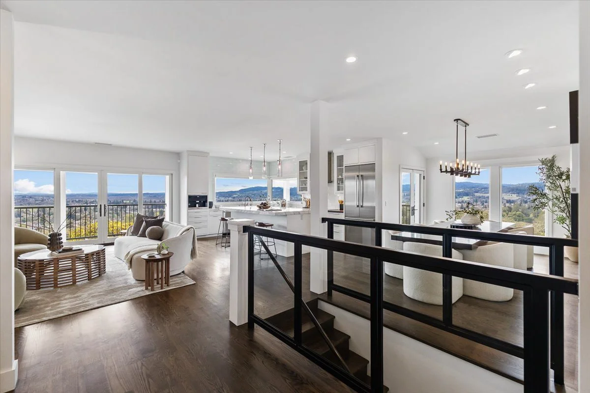 Bright, open-concept living room and kitchen with large windows showcasing a scenic view, modern white decor, wooden flooring, and contemporary furniture.