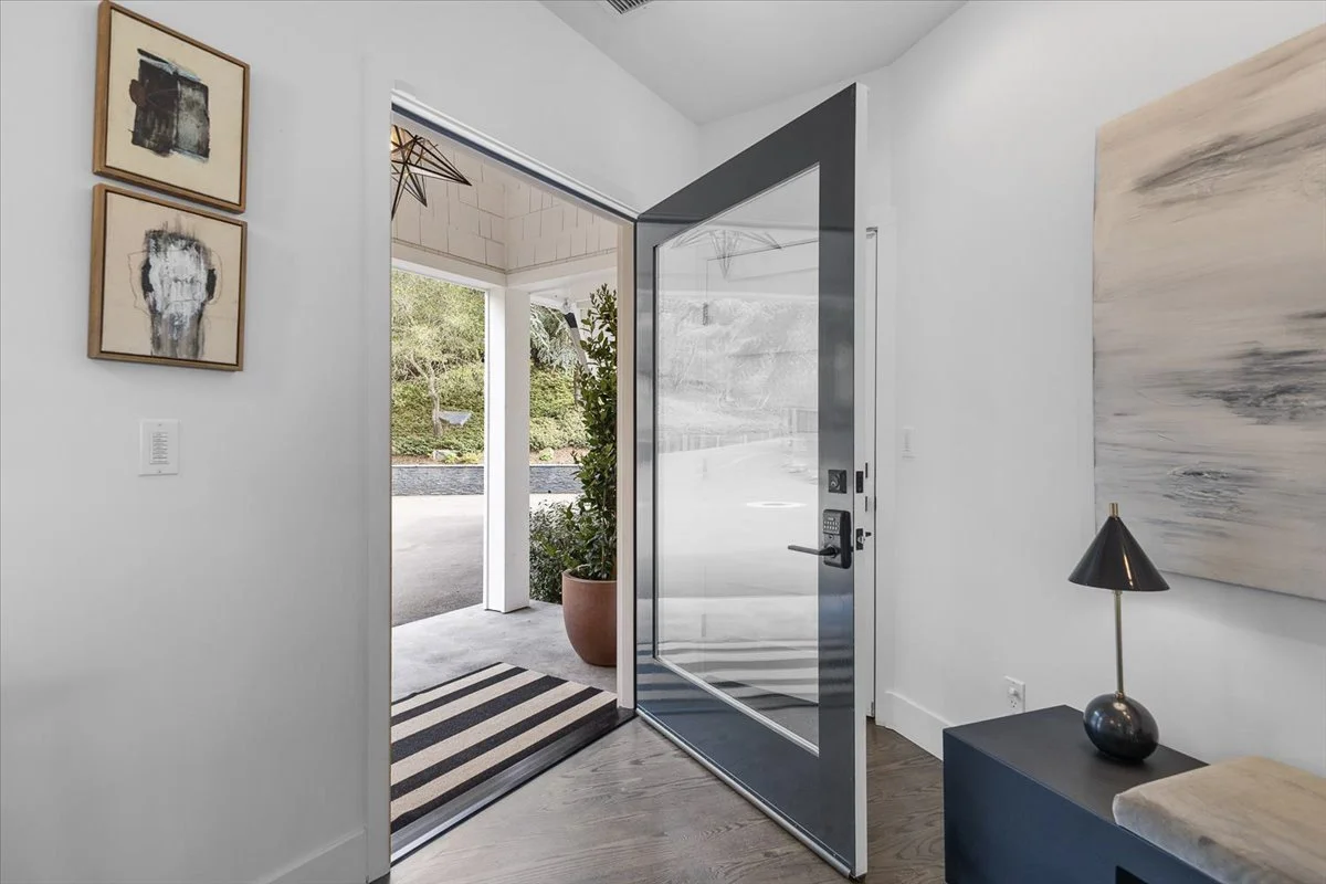 Entryway with a glass door, a striped rug on the floor, a potted plant outside, and wall art inside