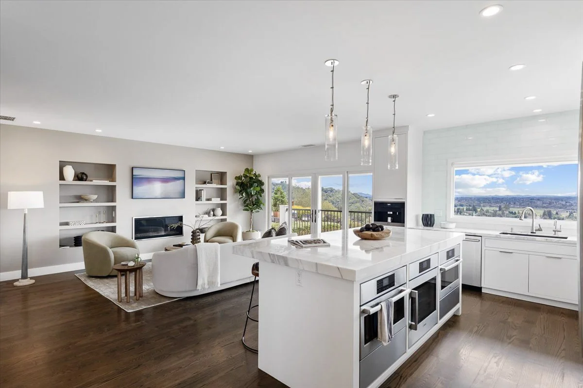 Open-concept living room and kitchen with white cabinetry, large window showing a valley view, and modern decor