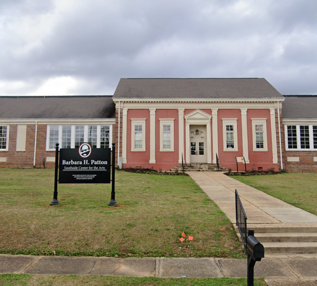 The Barbara H. Patton Southside Center for the Arts, a brick and pink-painted building with a walkway leading to the entrance, a black sign with white text, and cloudy sky overhead.