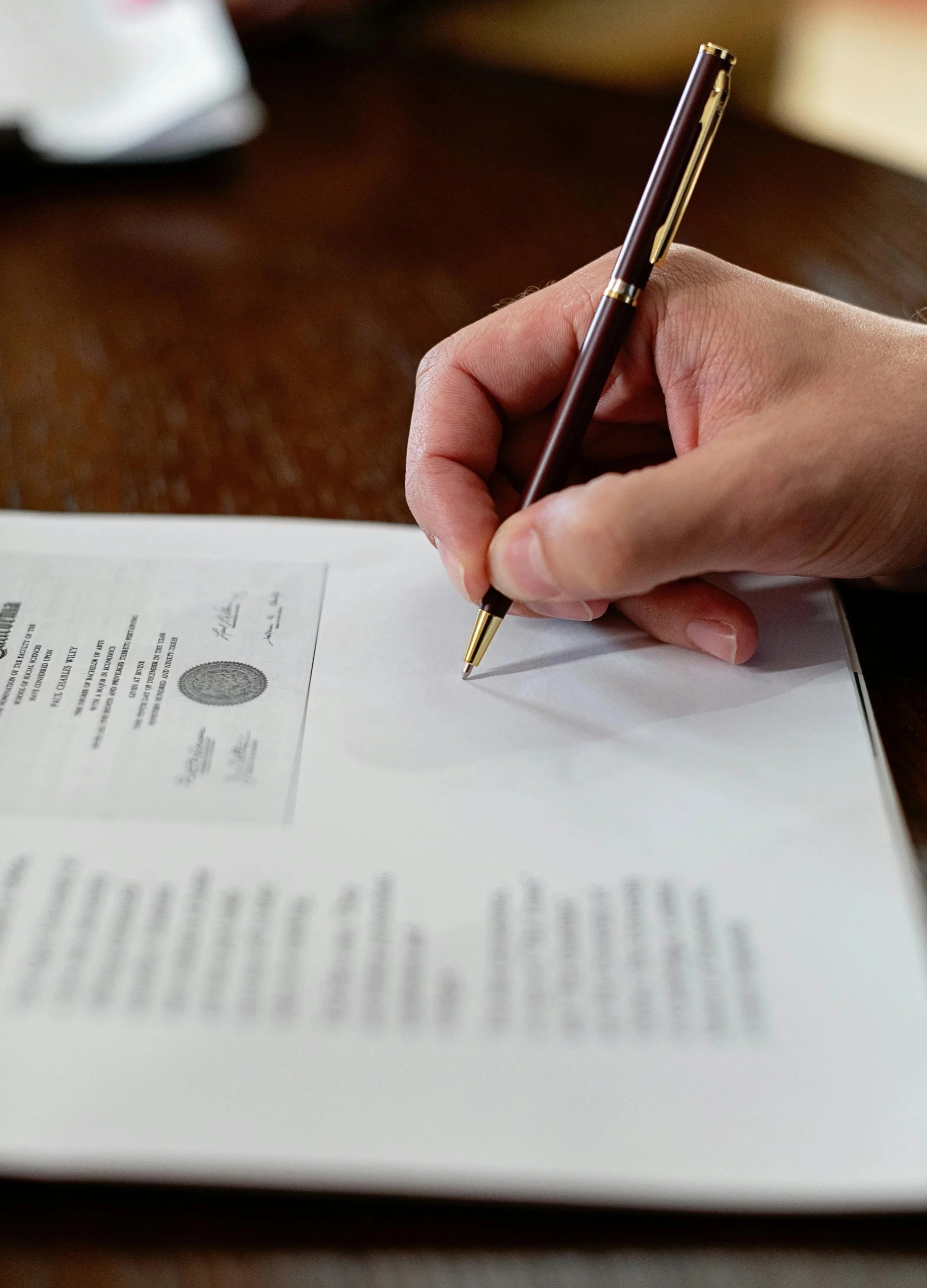 A person holding a pen and signing a document with official seals and signatures.