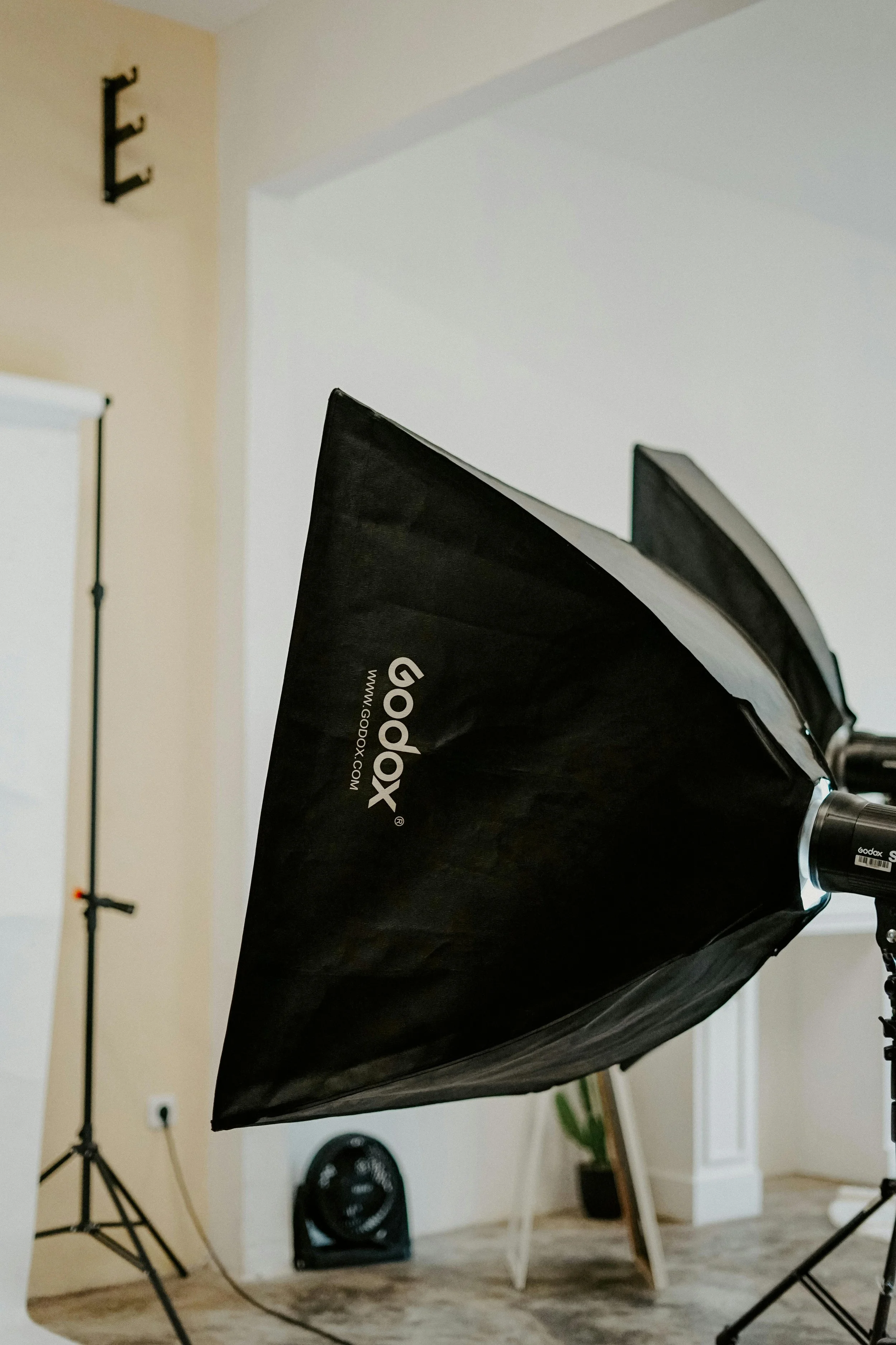 Photography studio with a Godox softbox, lighting equipment, and background setup including a white backdrop and a tripod.